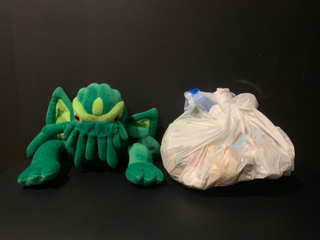 Small Cthulhu plush sits beside a kitchen-sized trash bag one-third full.